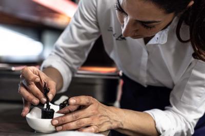 Un barman verse un liquide sombre d'une petite bouteille dans un verre à cocktail rempli d'une boisson mousseuse.