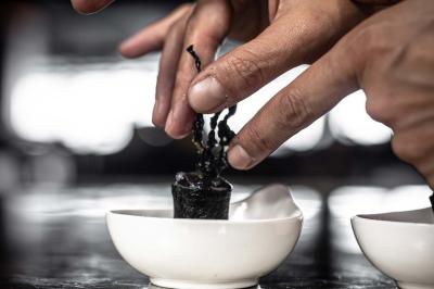Un barman verse un liquide sombre d'une petite bouteille dans un verre à cocktail rempli d'une boisson mousseuse.