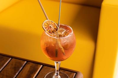 Un barman verse un liquide sombre d'une petite bouteille dans un verre à cocktail rempli d'une boisson mousseuse.