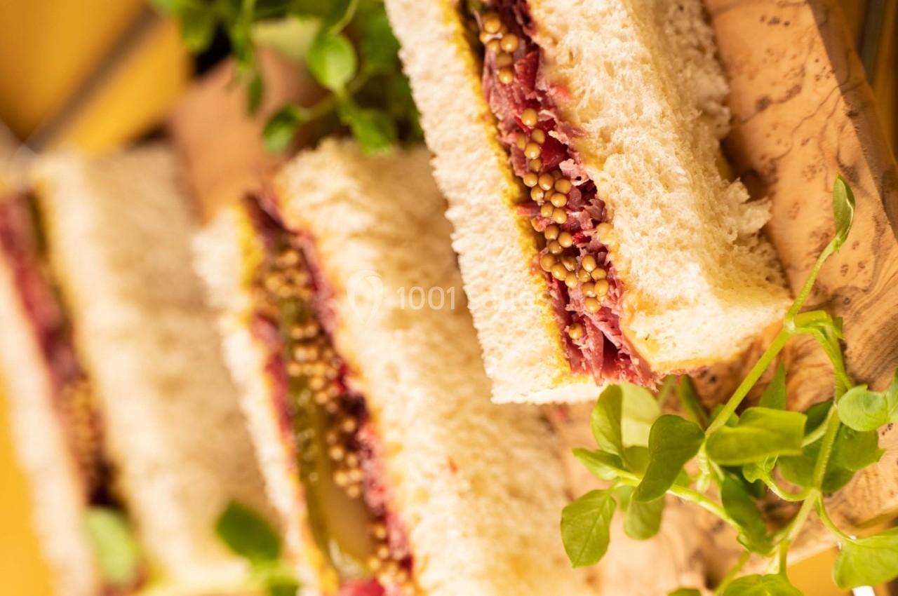 Tranches de sandwich garnies de viande, cornichons et moutarde, présentées sur une planche en bois avec des herbes fraîches.