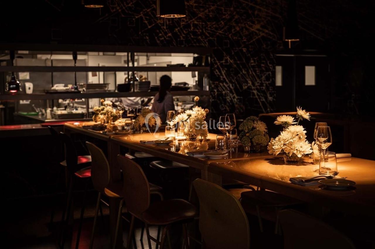 Table en bois éclairée avec des fleurs blanches, verres et couverts, dans un restaurant à l'ambiance tamisée.