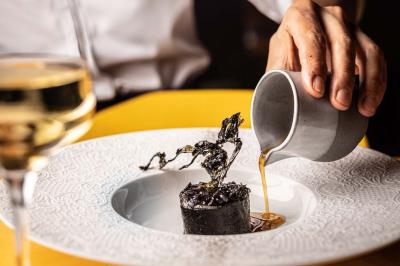 Un barman verse un liquide sombre d'une petite bouteille dans un verre à cocktail rempli d'une boisson mousseuse.