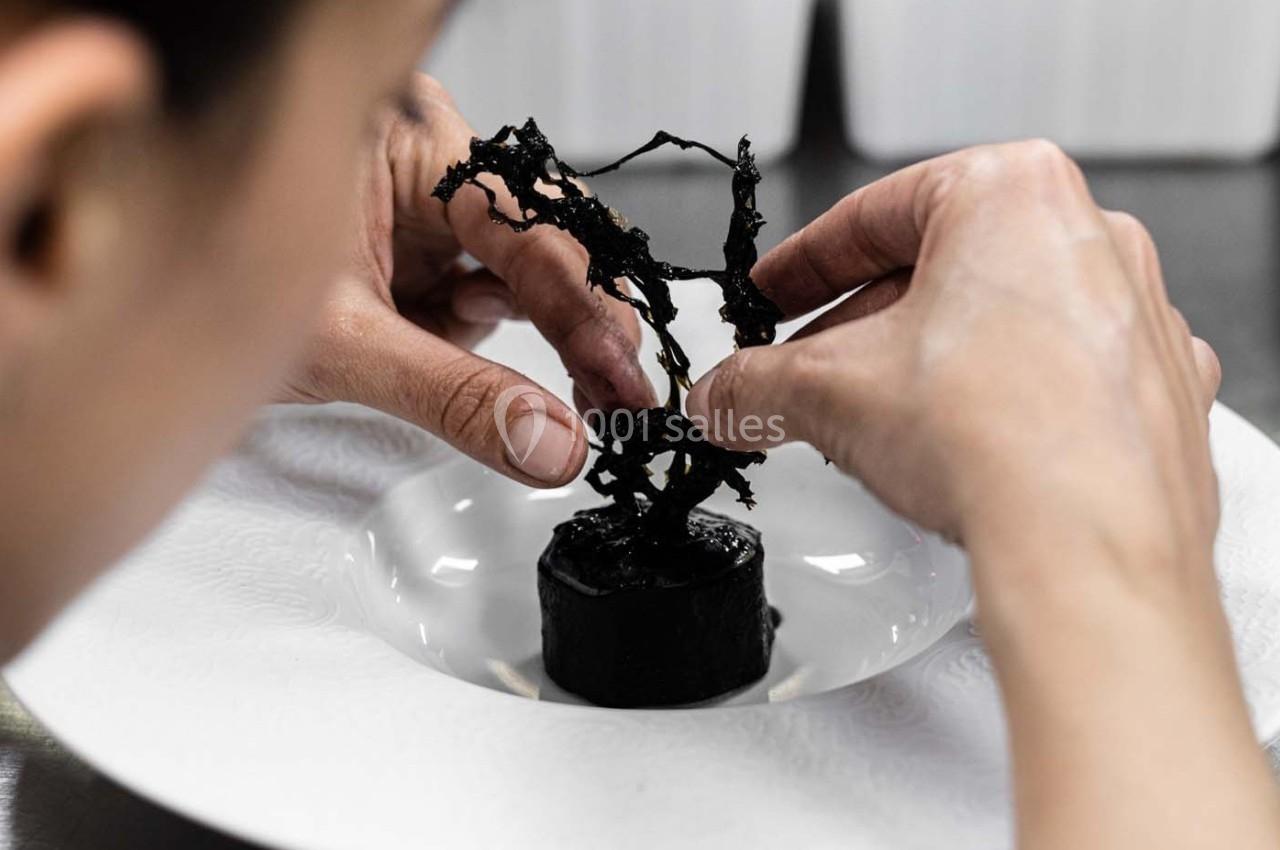 Une personne dispose délicatement une garniture noire sculpturale sur un plat blanc.
