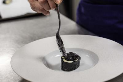 Un barman verse un liquide sombre d'une petite bouteille dans un verre à cocktail rempli d'une boisson mousseuse.