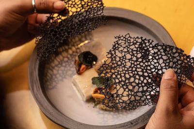 Un barman verse un liquide sombre d'une petite bouteille dans un verre à cocktail rempli d'une boisson mousseuse.