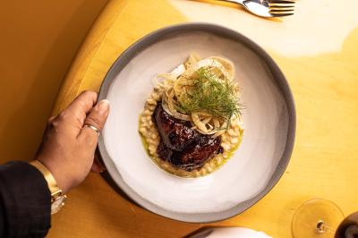 Un barman verse un liquide sombre d'une petite bouteille dans un verre à cocktail rempli d'une boisson mousseuse.