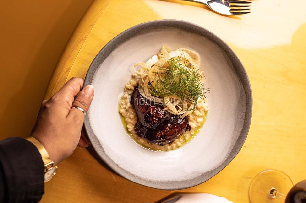 Assiette contenant un plat composé de viande braisée, purée crémeuse et garniture de fenouil, tenue par une main.