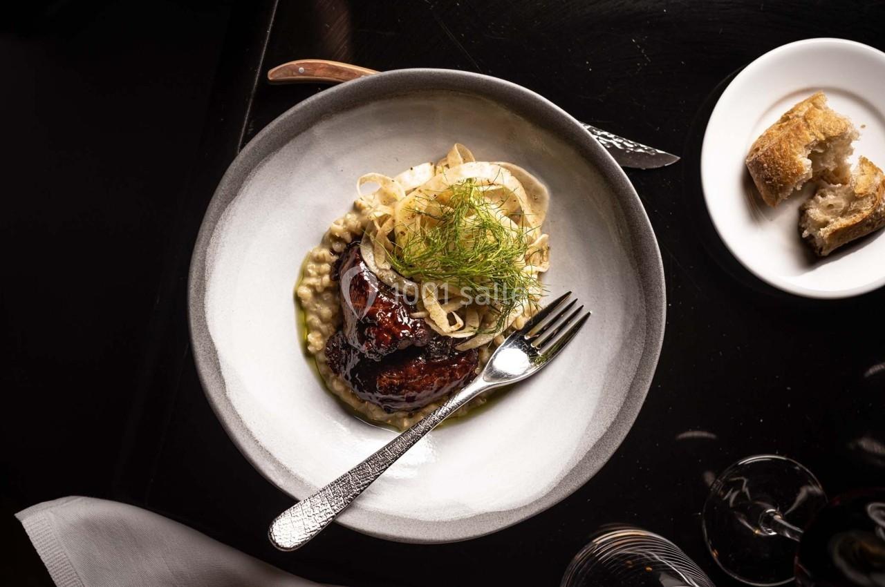 Assiette contenant un plat gastronomique avec viande glacée, purée crémeuse, fenouil et pain en accompagnement.