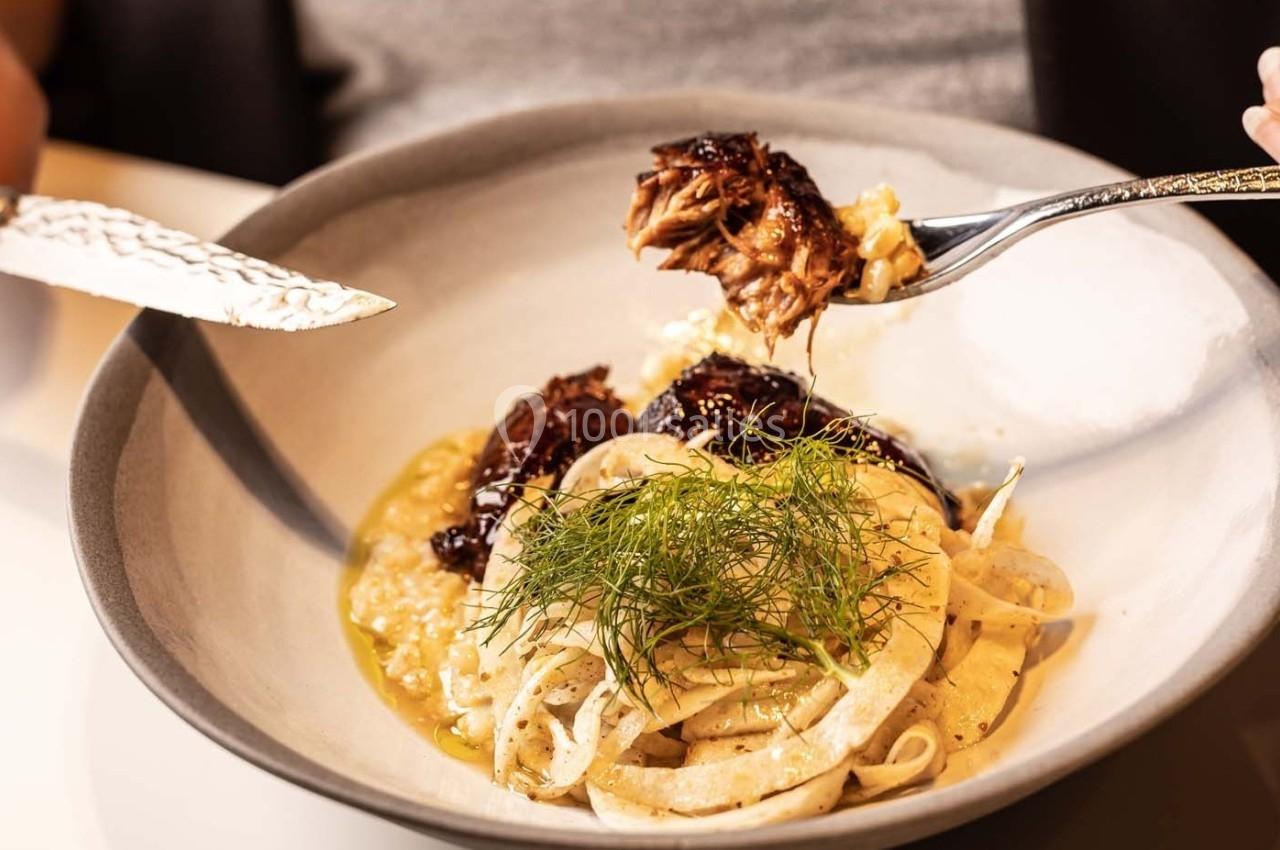 Assiette de pâtes garnie de viande effilochée, sauce et herbes fraîches, tenue par une personne avec une fourchette et un…