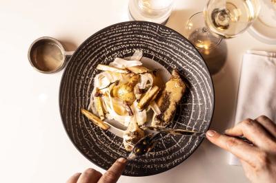 Un barman verse un liquide sombre d'une petite bouteille dans un verre à cocktail rempli d'une boisson mousseuse.
