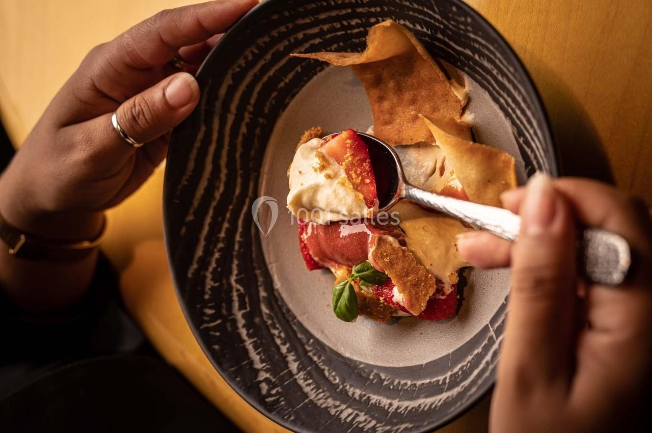 Une personne déguste un dessert composé de fruits rouges, crème et croustillants dans une assiette sombre.