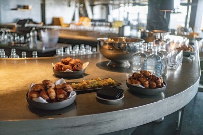 Un barman verse un liquide sombre d'une petite bouteille dans un verre à cocktail rempli d'une boisson mousseuse.