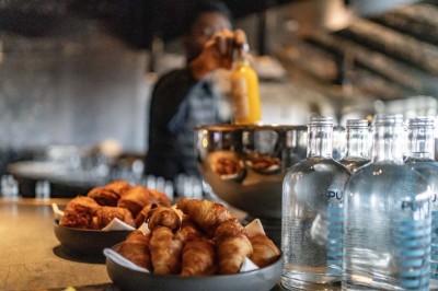 Un barman verse un liquide sombre d'une petite bouteille dans un verre à cocktail rempli d'une boisson mousseuse.