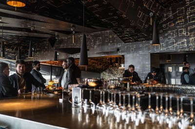 Un barman verse un liquide sombre d'une petite bouteille dans un verre à cocktail rempli d'une boisson mousseuse.