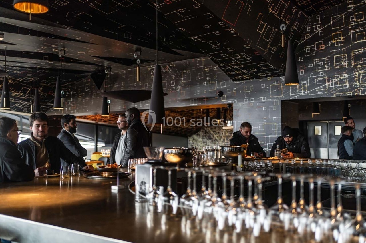 Des personnes discutent autour d'un bar moderne avec un éclairage tamisé et une décoration géométrique sombre.