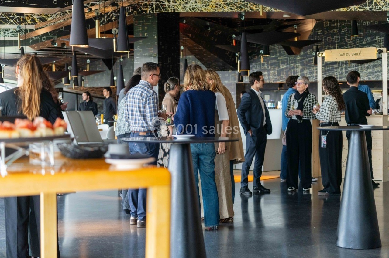 Groupe de personnes discutant debout dans un espace intérieur moderne avec tables et buffet en arrière-plan.