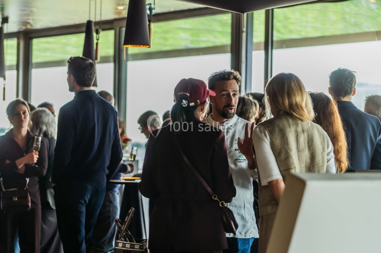 Groupe de personnes discutant dans un espace lumineux avec de grandes fenêtres et des tables en arrière-plan.