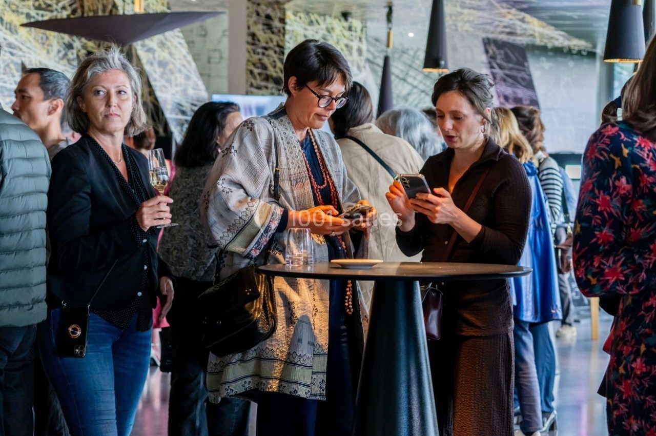 Des personnes discutent et consultent leurs téléphones autour d'une table haute lors d'un événement en intérieur.