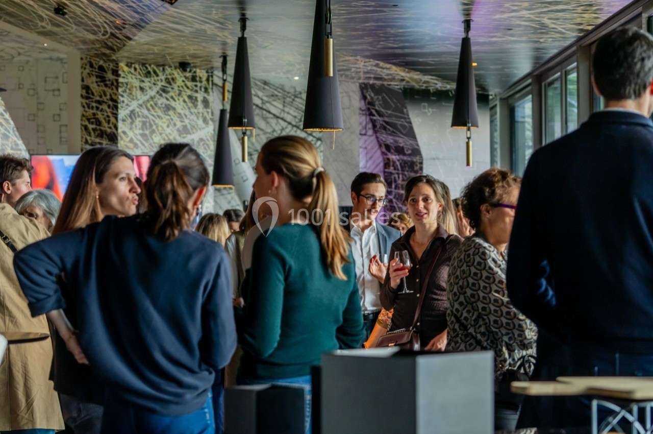 Groupe de personnes discutant dans un espace intérieur moderne avec éclairage suspendu et grandes fenêtres.