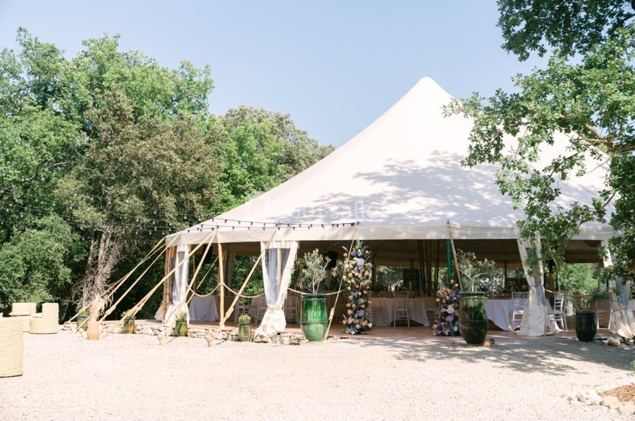 Tente blanche de style chapiteau installée en extérieur, entourée de végétation et décorée pour un événement.