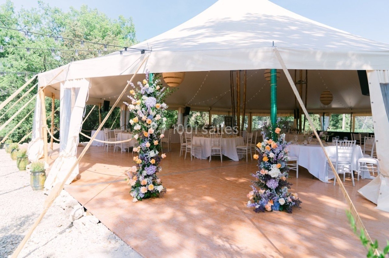Tente blanche décorée pour un événement, avec des tables dressées et des colonnes de fleurs colorées à l'entrée.