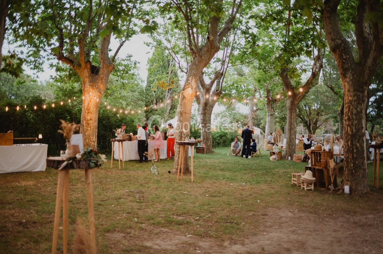 Jardin avec des arbres, guirlandes lumineuses et invités rassemblés autour de tables lors d'un événement en plein air.