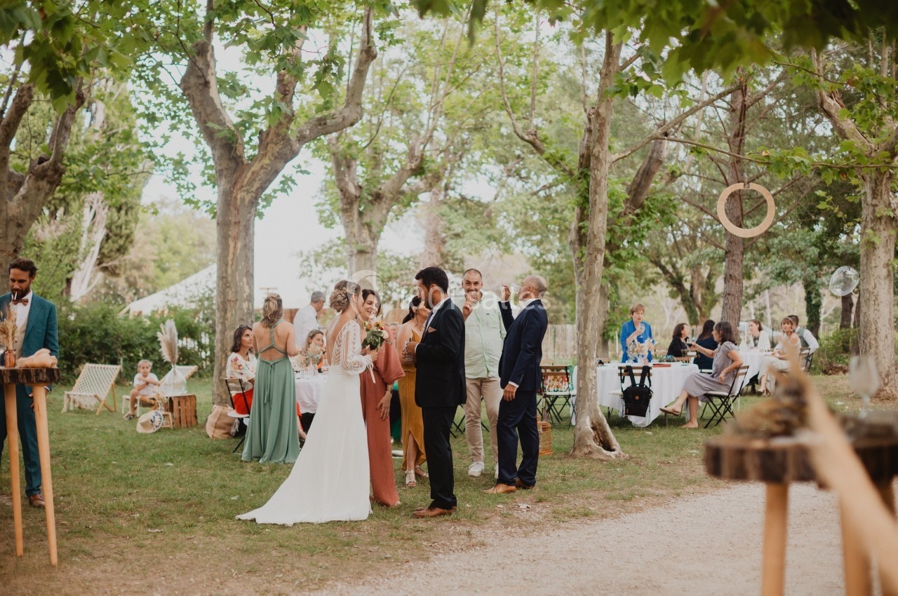 Un mariage en plein air avec des invités discutant sous des arbres, tables dressées en arrière-plan.