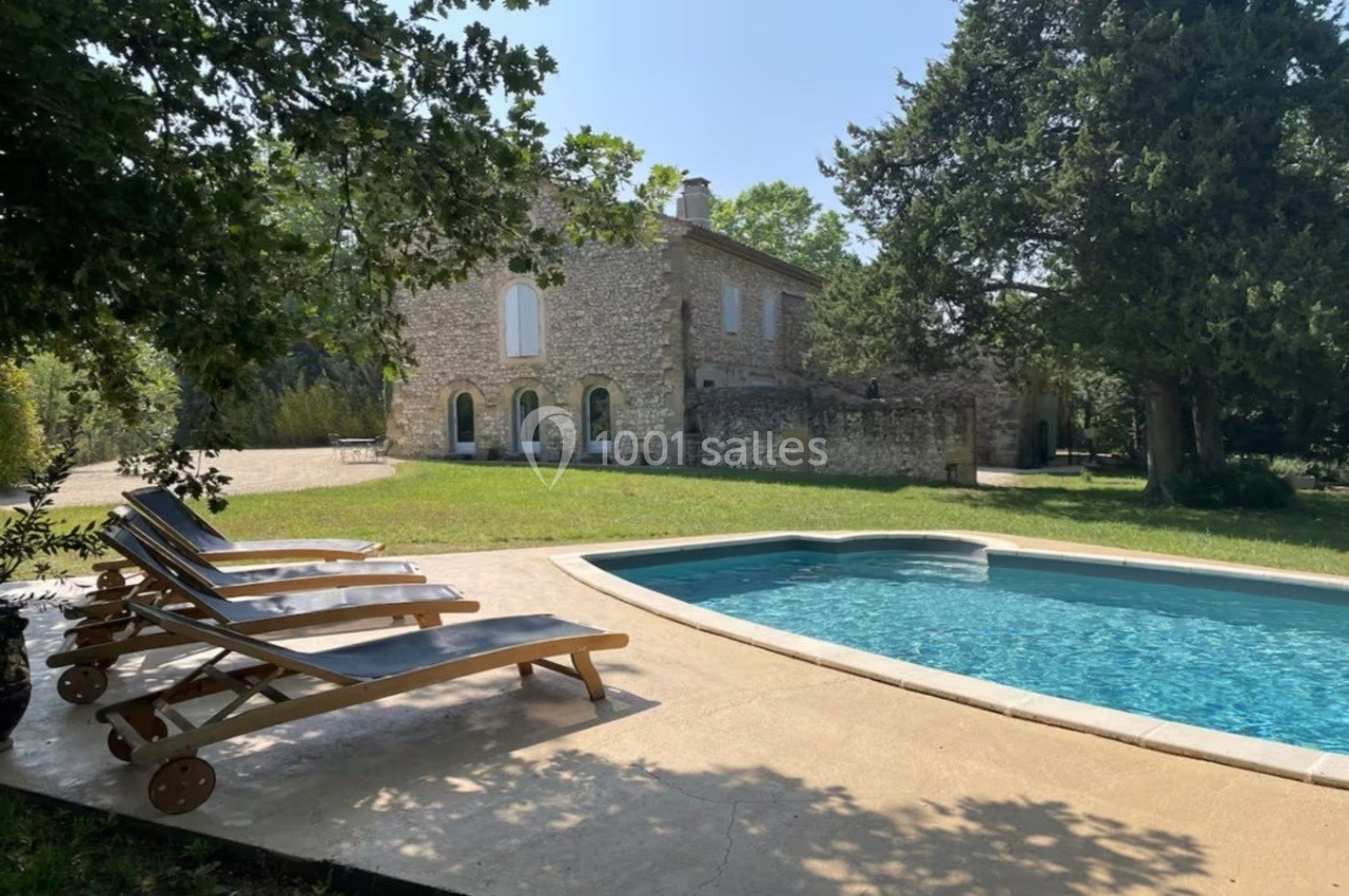 Maison en pierre entourée de verdure avec une piscine et des chaises longues sur une terrasse ensoleillée.