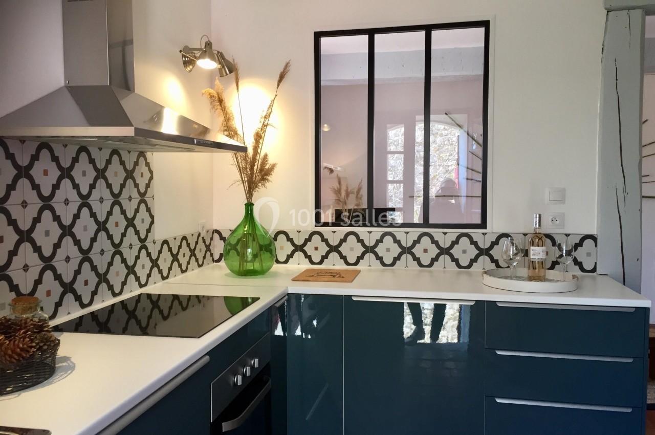 Cuisine moderne avec meubles bleu foncé, crédence à motifs, plan de travail blanc et verrière intérieure noire.