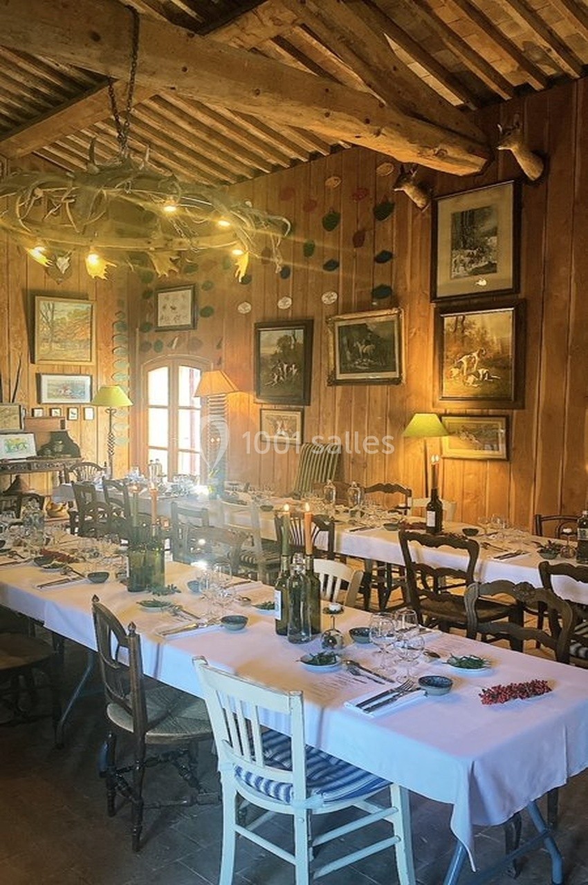 Salle à manger rustique avec de grandes tables dressées, des chaises dépareillées et des murs ornés de cadres.