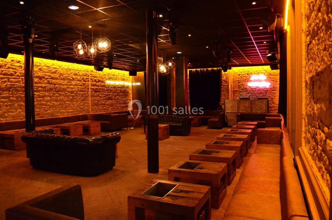 Salle avec murs en pierre, banquettes en cuir, tables basses en bois et éclairage tamisé.