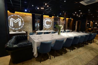 Salle de réunion avec tables dressées, chaises noires, murs en pierre et éclairage tamisé.