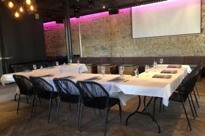 Salle de réunion avec tables dressées, chaises noires, murs en pierre et éclairage tamisé.