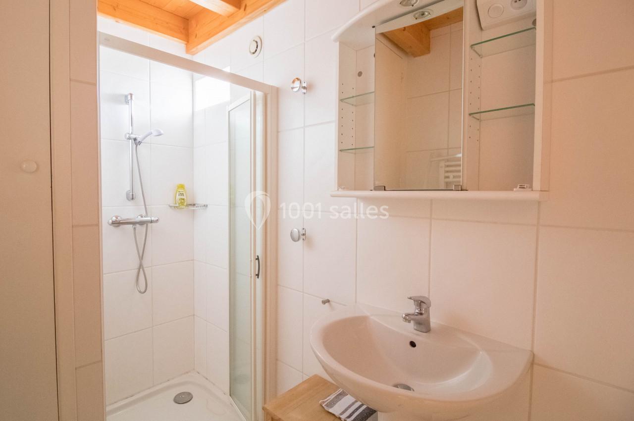 Salle de bain lumineuse avec douche à paroi vitrée, lavabo blanc, miroir avec étagères et plafond en bois.