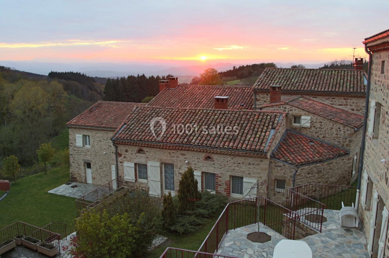 Vue d'un ensemble de maisons en pierre avec toits en tuiles, entourées de verdure, au coucher du soleil.