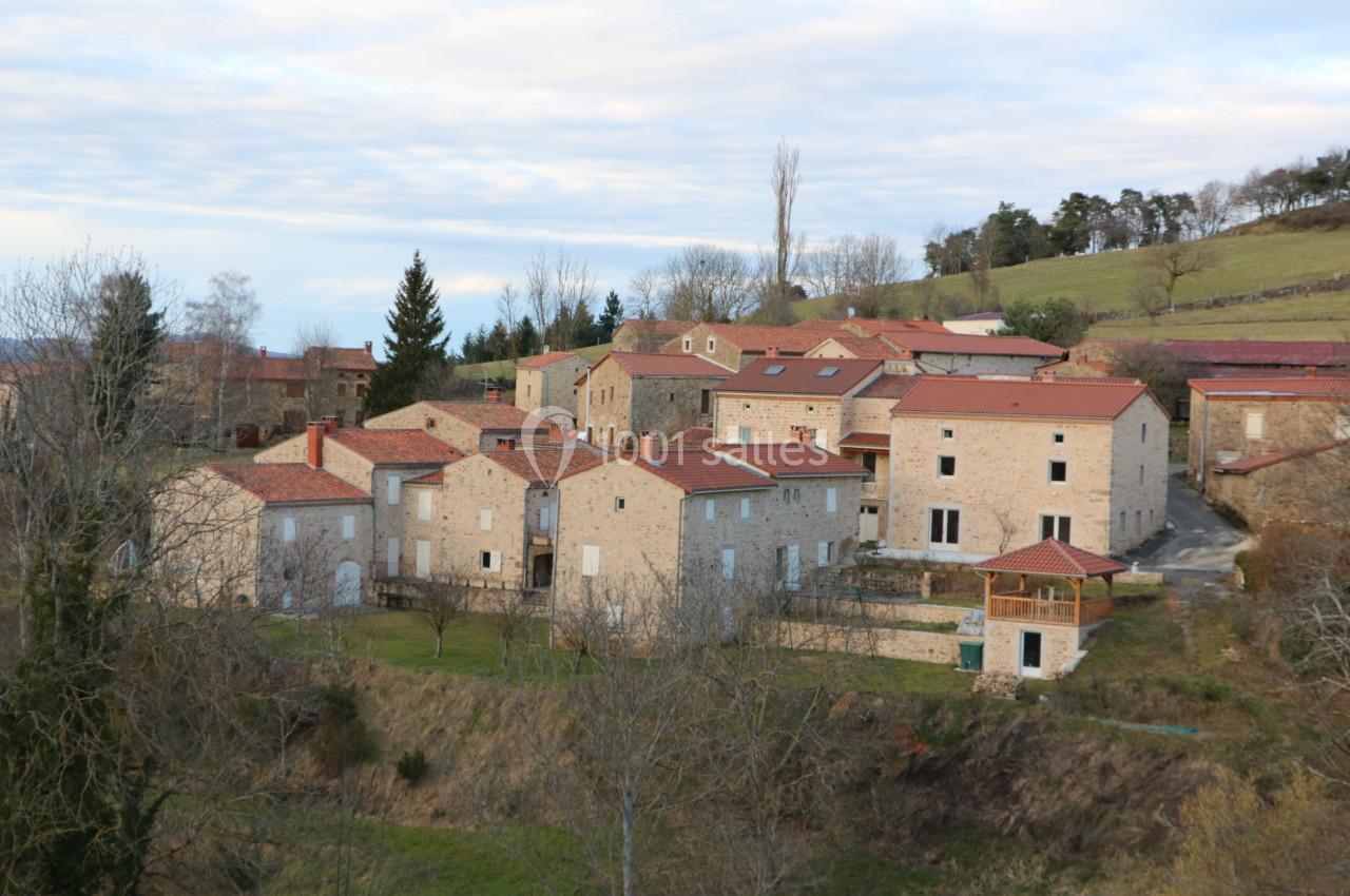Vue d'un village rural avec des maisons en pierre aux toits rouges, entouré de collines et d'arbres en hiver.