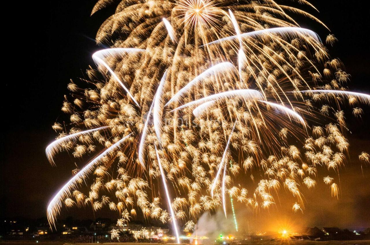 Feu d'artifice illuminant le ciel nocturne au-dessus d'une rivière, avec des reflets lumineux sur l'eau.