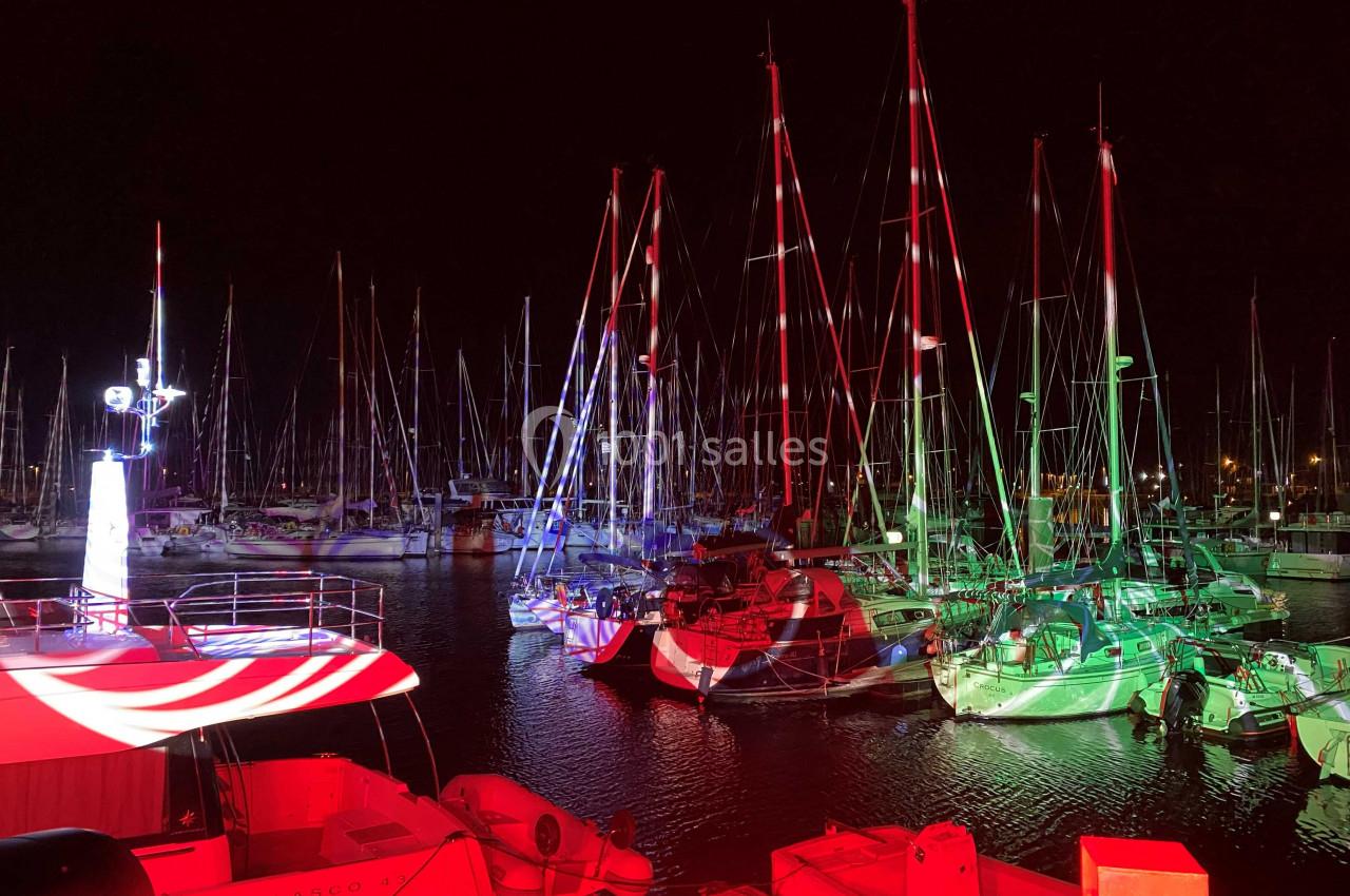 Voiliers amarrés dans un port de nuit, éclairés par des lumières rouges et vertes.