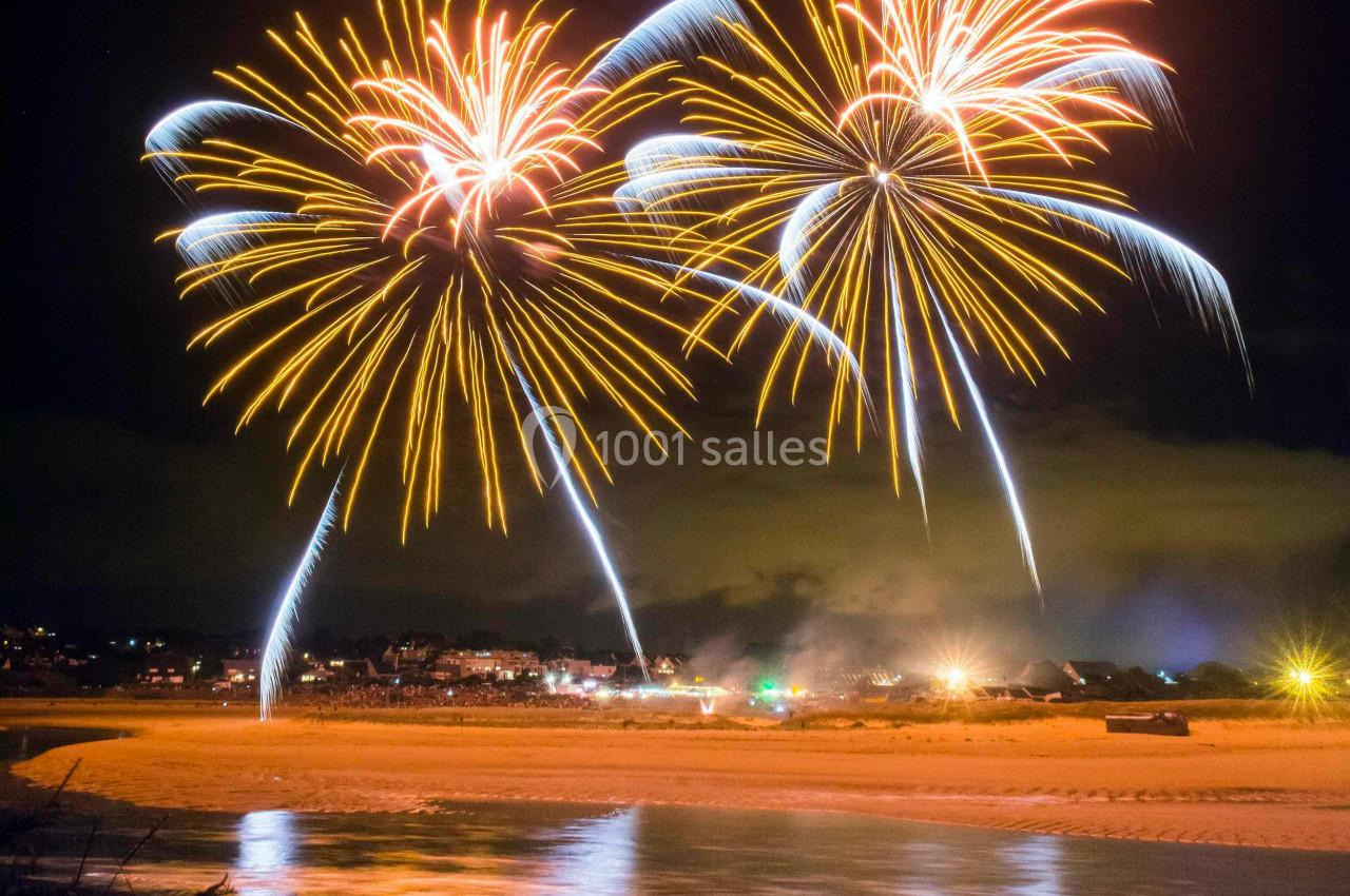 Feux d'artifice colorés illuminant le ciel nocturne au-dessus d'une plage avec leur reflet dans l'eau.
