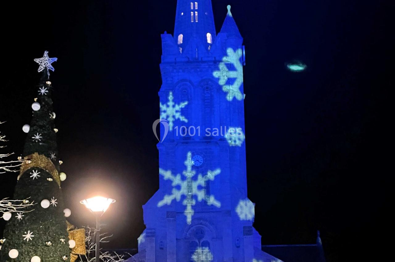 Église illuminée en bleu avec des motifs de flocons de neige, décorations de Noël et sculptures au premier plan.