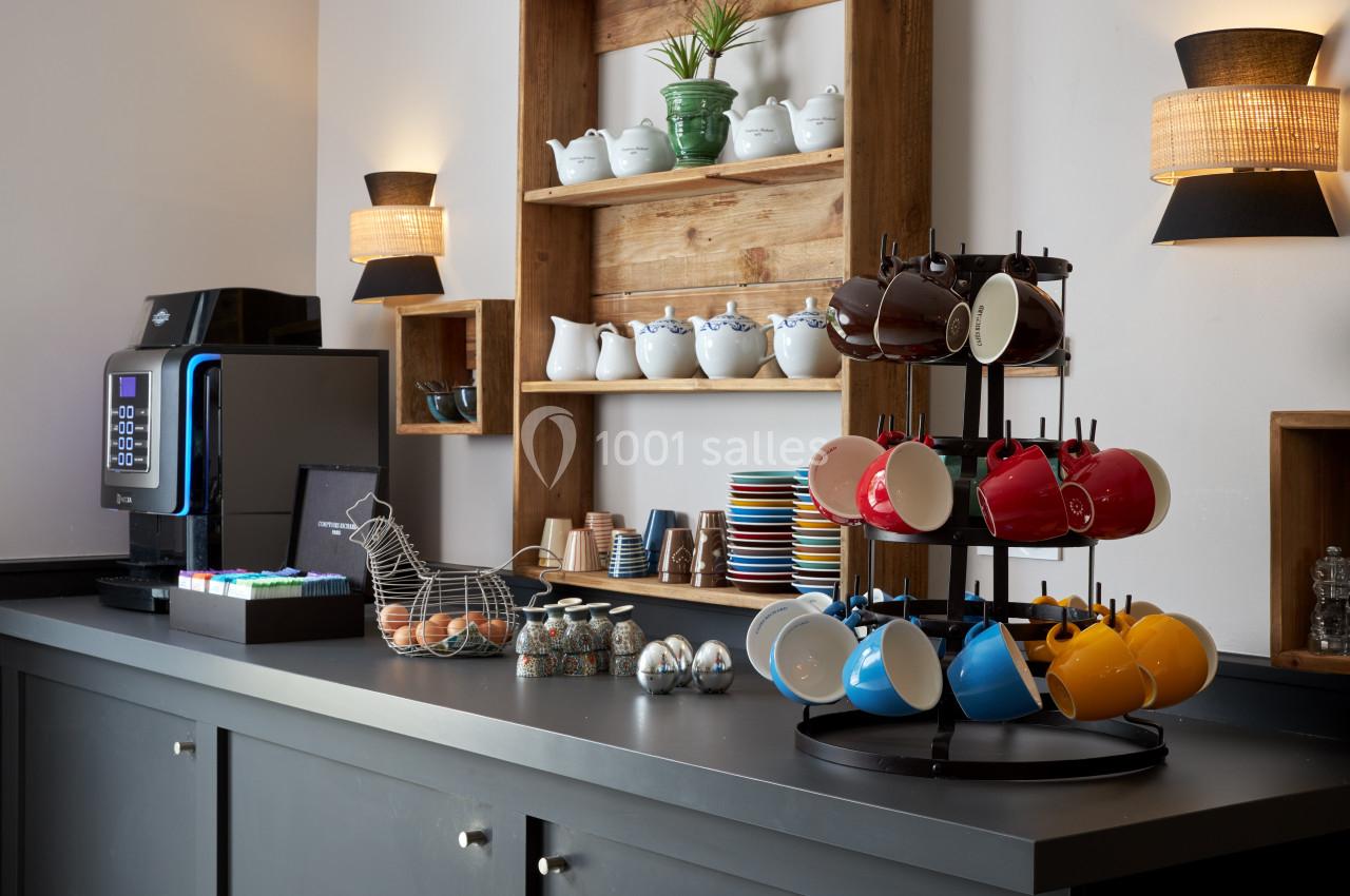Comptoir avec machine à café, tasses colorées, pots en céramique et étagères décorées d'objets assortis.