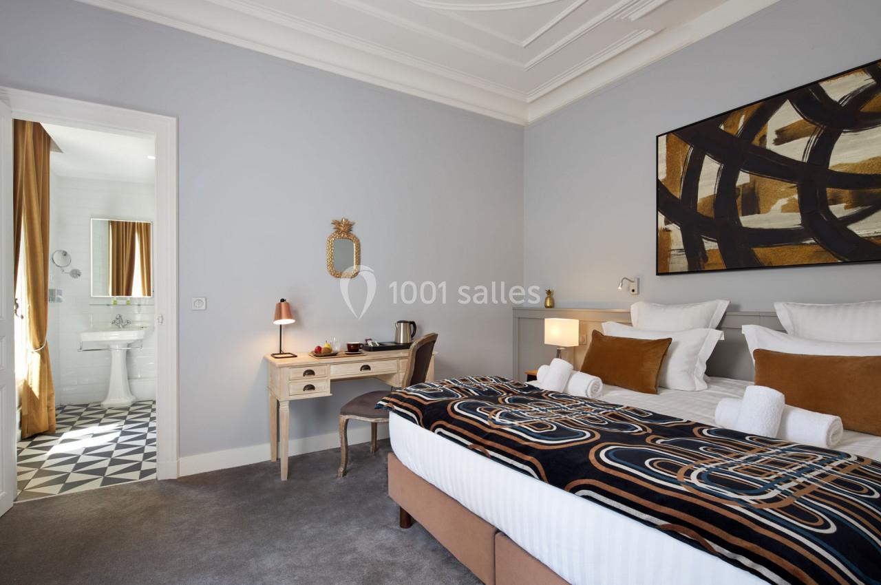 Chambre lumineuse avec lit double, bureau, salle de bain attenante et décoration moderne aux tons neutres et chaleureux.