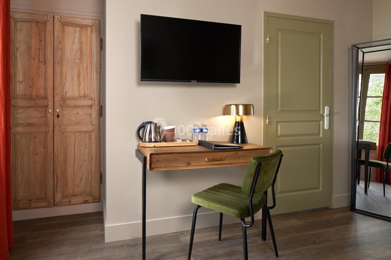 Bureau en bois avec chaise verte, lampe dorée, téléviseur mural, et plateau avec bouilloire et bouteilles d'eau.