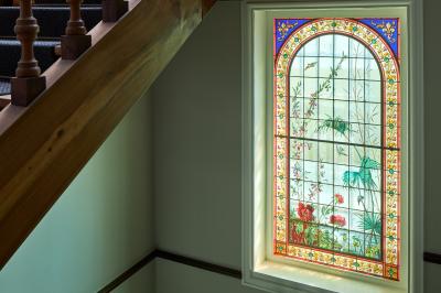 Escalier en bois avec une fenêtre en vitrail coloré représentant des motifs floraux et végétaux.