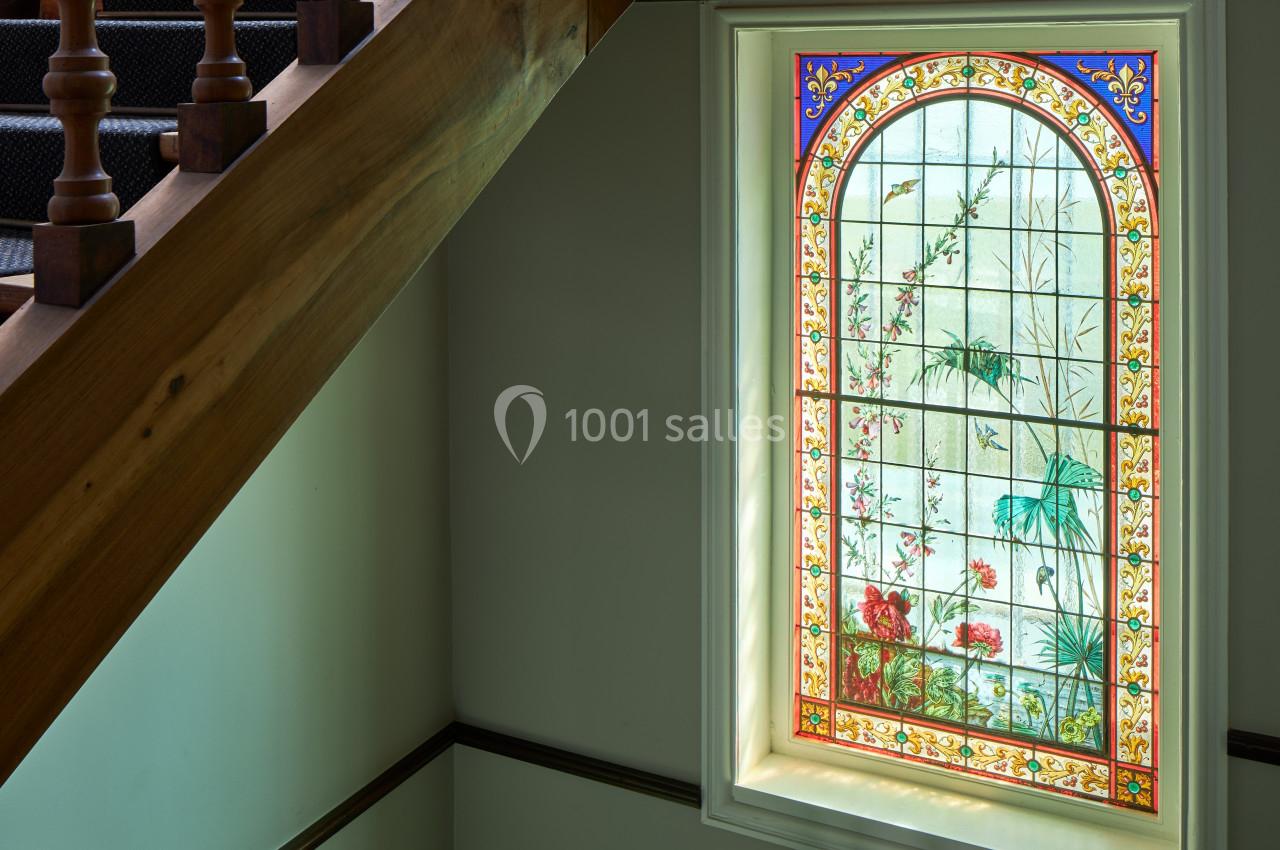 Escalier en bois avec une fenêtre en vitrail coloré représentant des motifs floraux et végétaux.