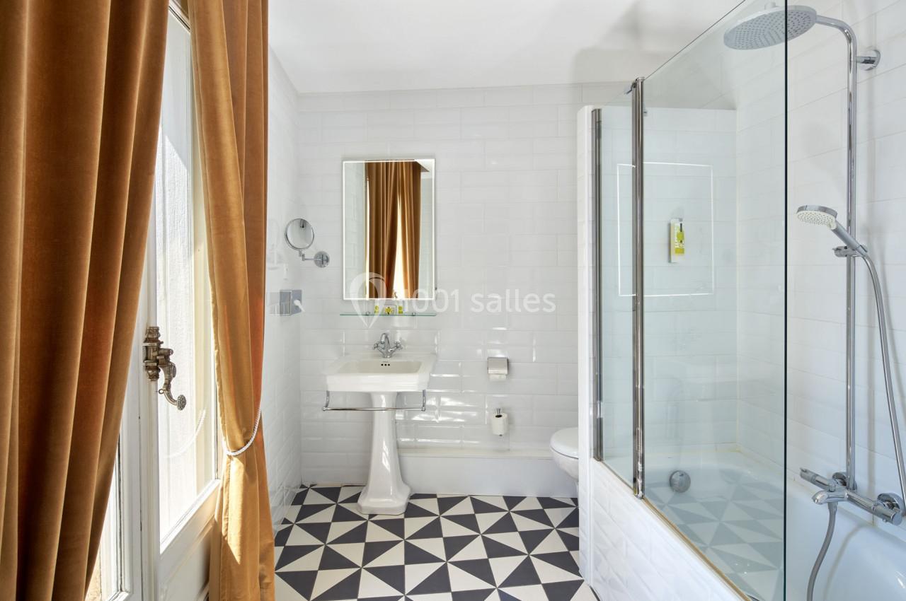 Salle de bain lumineuse avec carrelage géométrique, baignoire avec paroi vitrée, lavabo et rideaux marron.