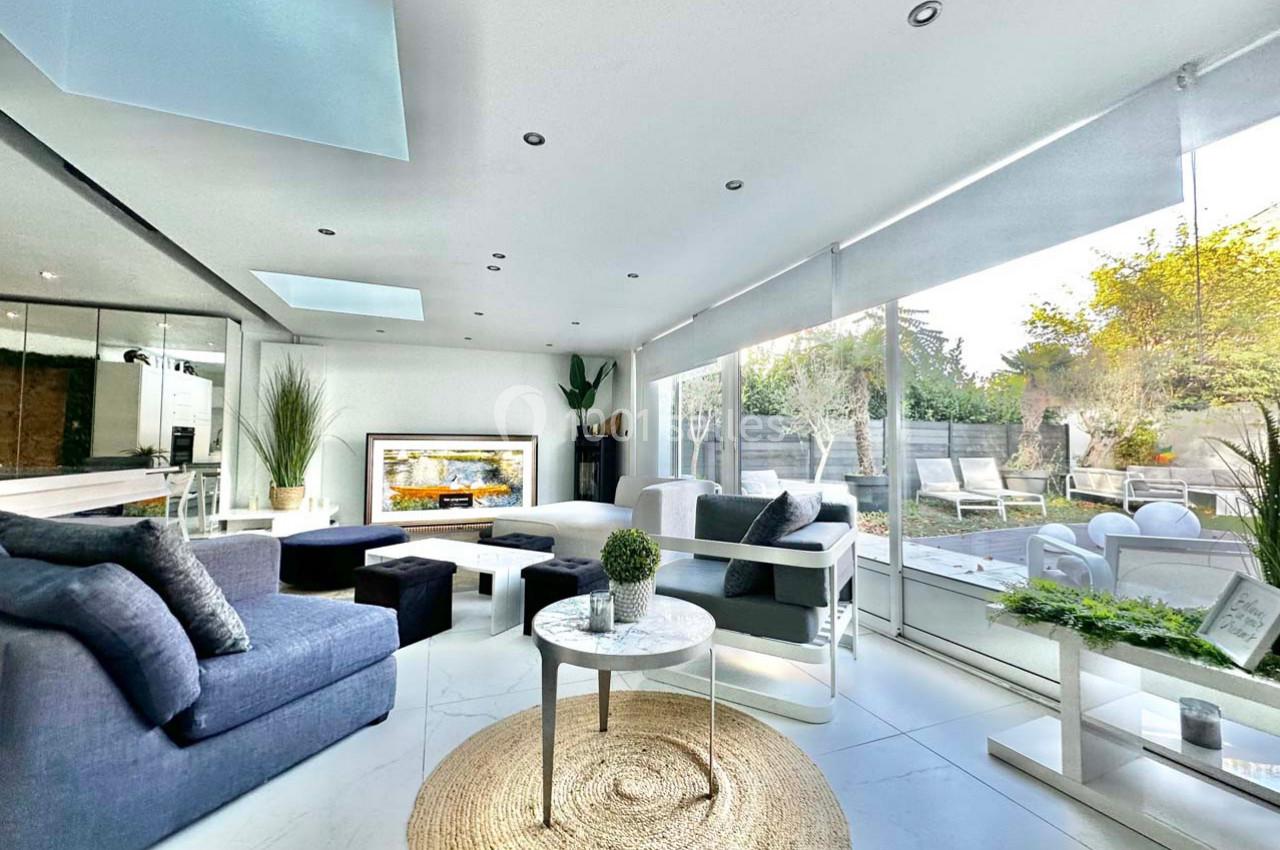 Salon moderne avec canapé bleu, table basse, grandes baies vitrées donnant sur une terrasse et jardin lumineux.