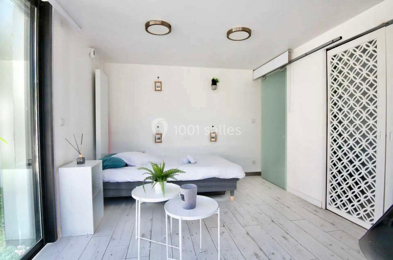 Chambre lumineuse avec lit double, tables basses, porte coulissante en verre et sol en bois clair.