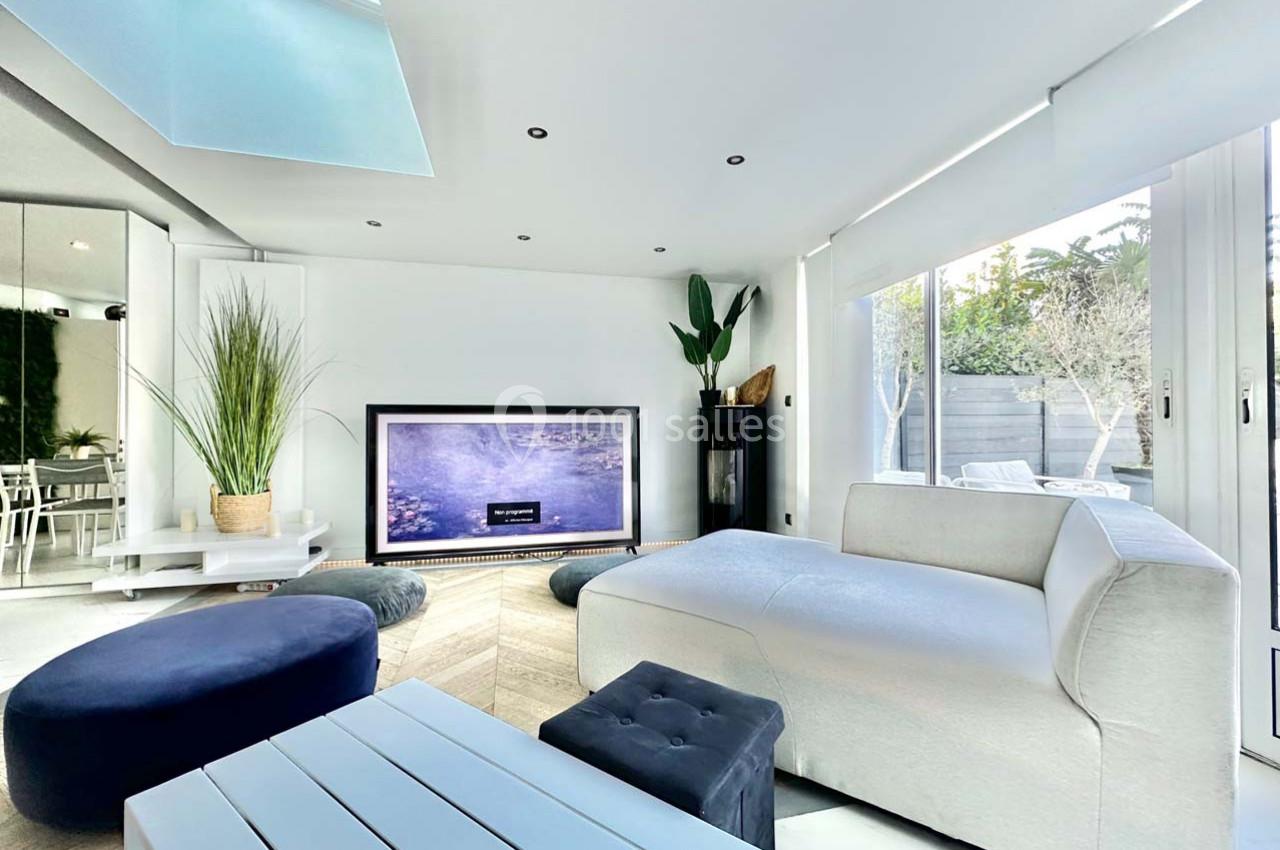 Salon moderne avec canapé blanc, table basse, plantes décoratives et grande baie vitrée donnant sur un jardin.