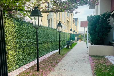 Allée extérieure éclairée par des lampadaires, bordée de bancs, d'arbustes et d'un parterre de fleurs.